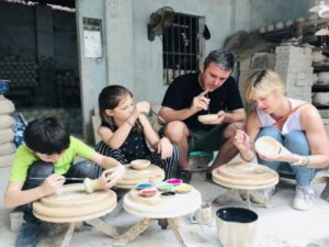A family learning to paint pottery bowls during a traditional Bat Trang ceramic workshop.