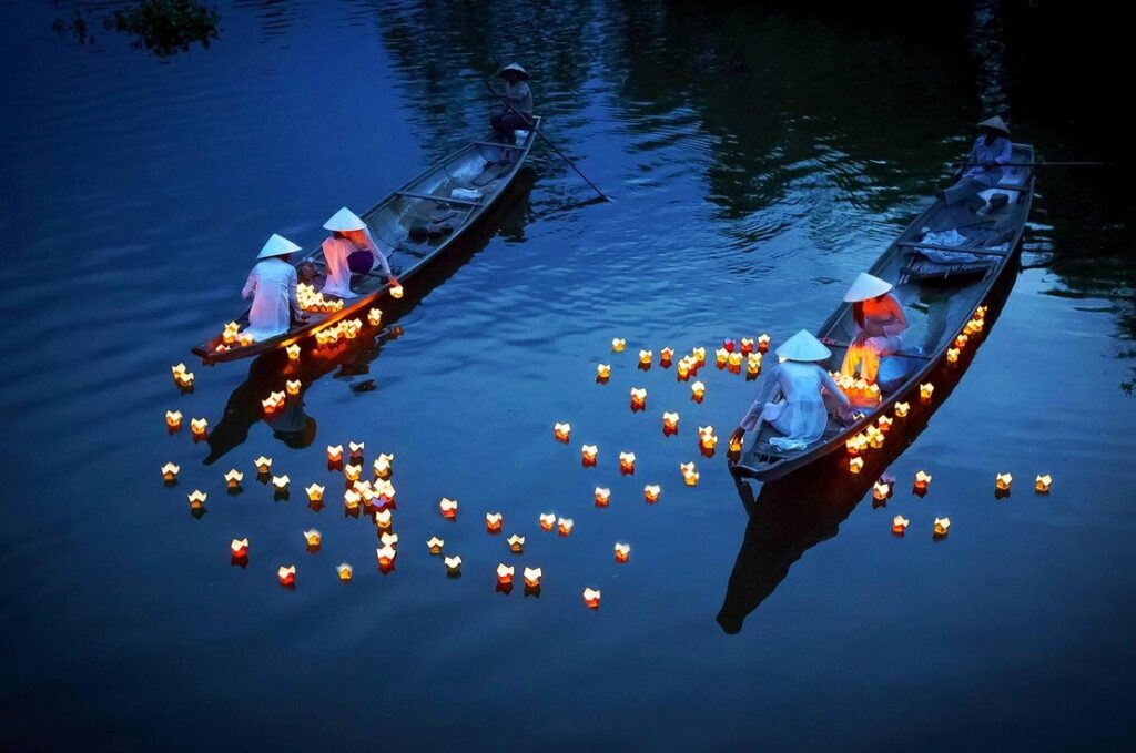 People paddling small boats and releasing glowing lanterns onto a quiet river.