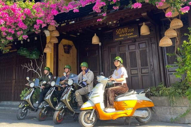 Travelers riding Vespas through Hoi An Old Town with colorful bougainvillea.