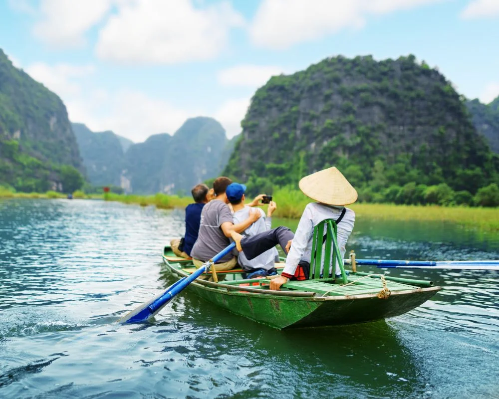 Tourists on a small rowing boat passing through the limestone mountains of Ninh Binh.