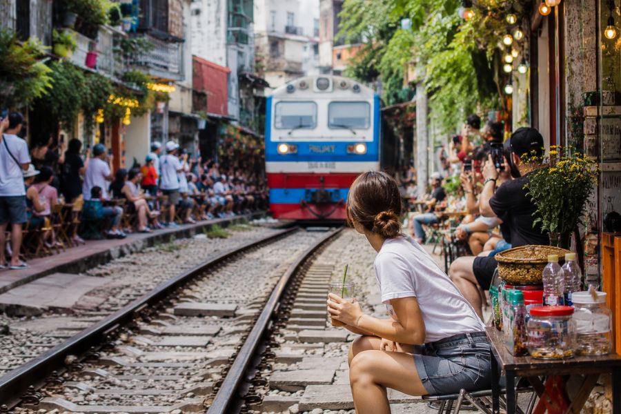 Traveler sitting at Hanoi Train Street while a train approaches